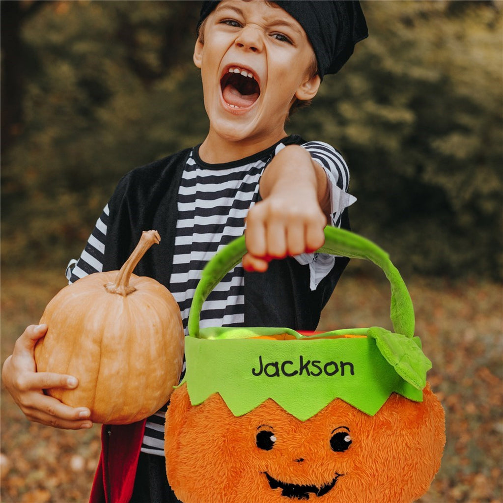 Child holding personalized trick or treat candy basket shaped like a smiling pumpkin with name Jackson