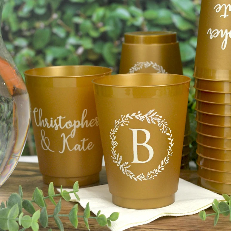Gold frosted 16 ounce plastic cups personalized with 'Wreath Initial 'B' design on the front and 2 lines of print on the back in ivory imprint color