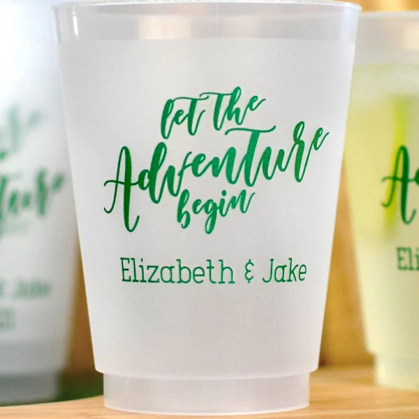 Clear frosted 16 oz. wedding drink cups personalized with 'Let The Adventure Begin' design and bride and groom's name in green imprint color