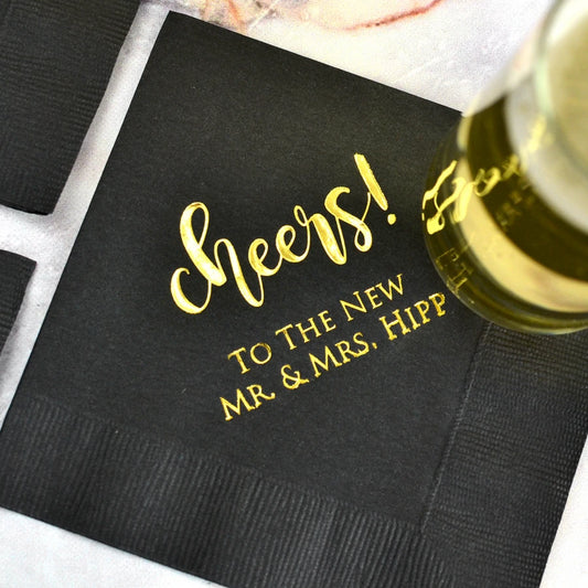 Beverage glass sitting on black color wedding beverage napkin personalized cheers design and 2 lines of custom text in gold print