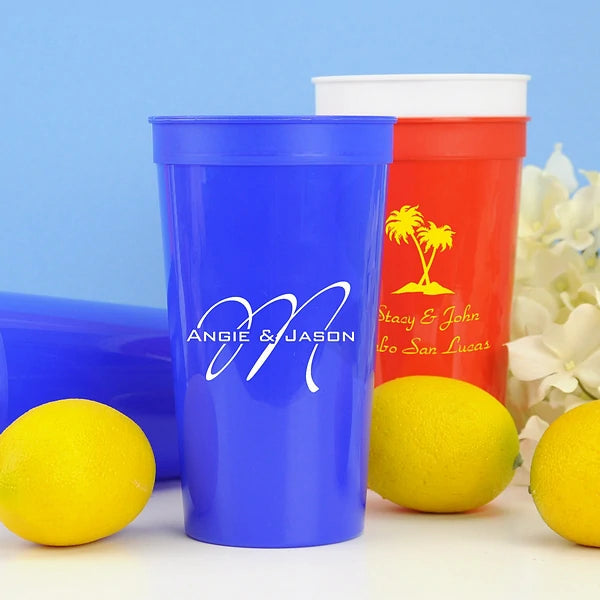 Blue 22 oz. stadium wedding cup personalized with custom wedding monogram in white imprint color and red cup personalized with 'Palm Trees' design and 2 lines of text in yellow imprint color
