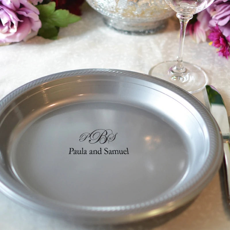 Silver plastic dinner plate personalized with wedding monogram and bride and groom name in black print on wedding reception dinner table