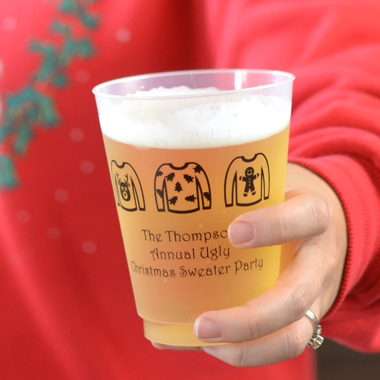 Person holding Christmas party beer cup personalized with ugly sweater design and 3 lines of custom text in black print