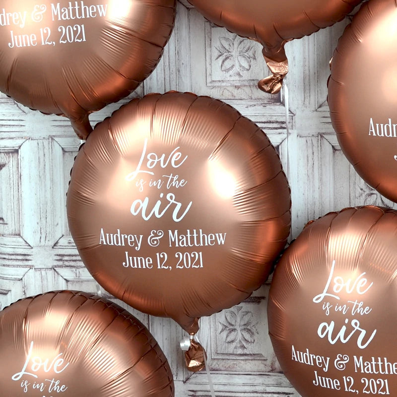 Luxe rose gold color round mylar wedding balloons personalized with love is in the air design and custom text in white print