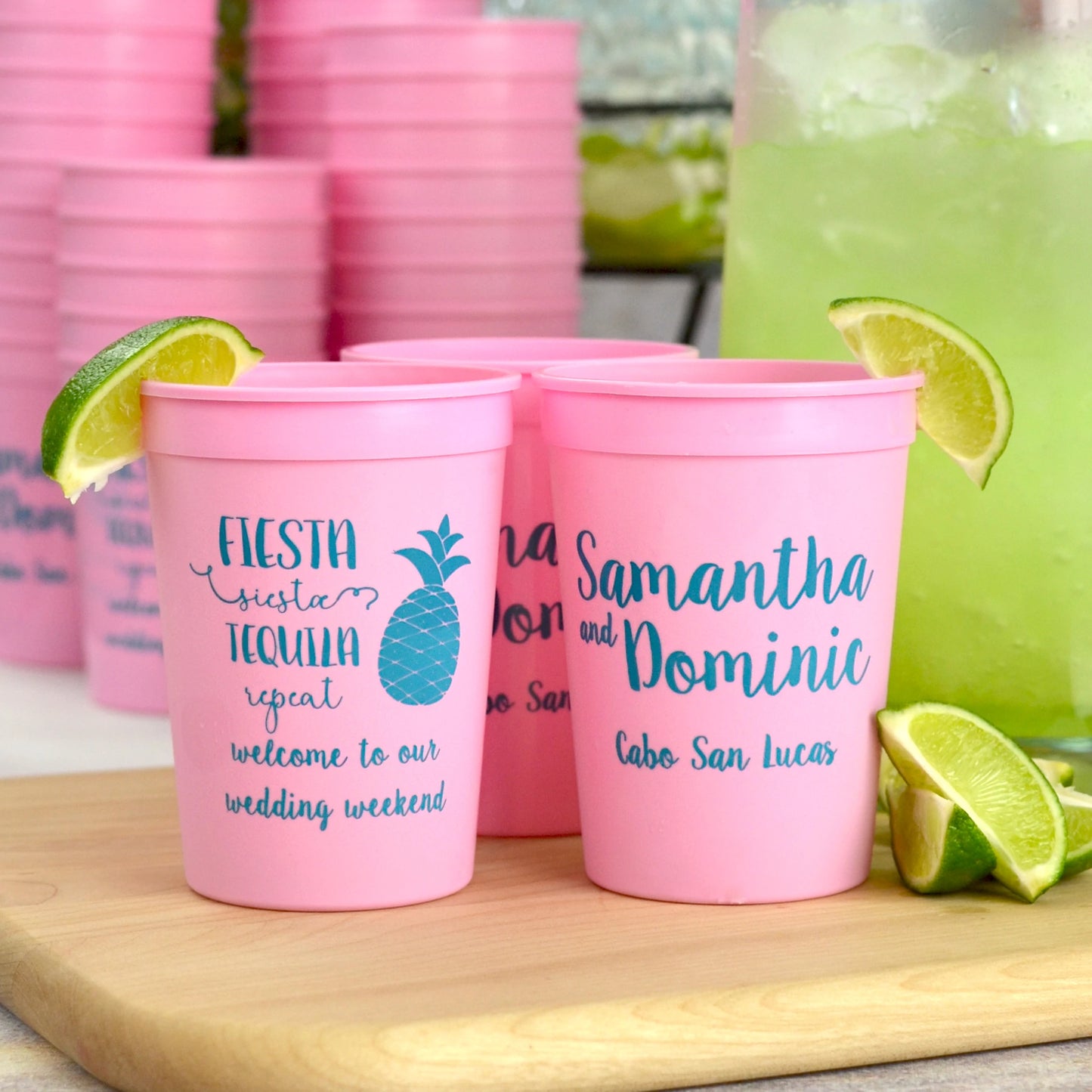Pink 12 oz. stadium wedding cups personalized with fiesta tequila design and two lines of text on the front and bride and groom names and wedding destination on the back in turquoise print